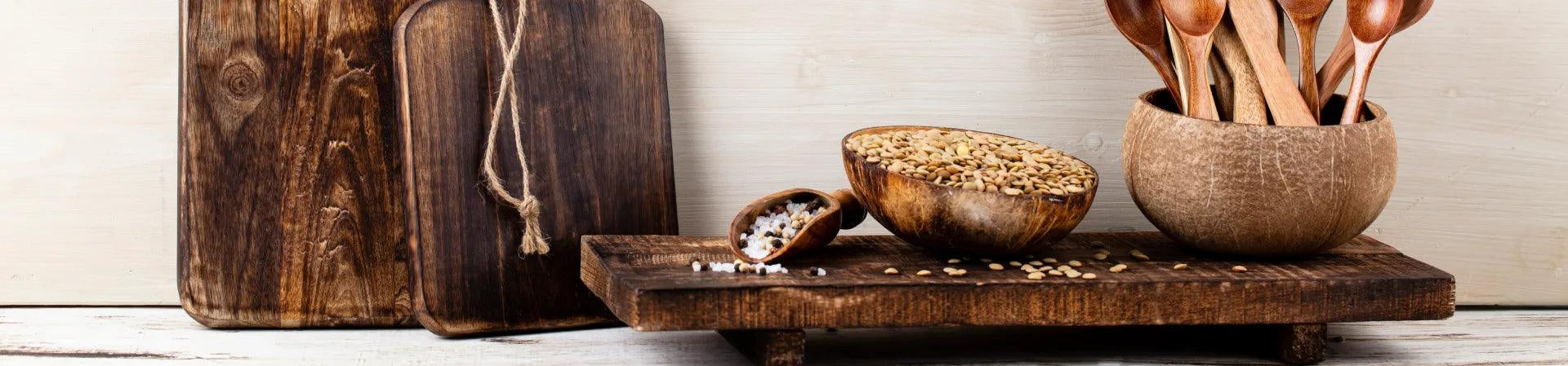 Handmade teak wood kitchen accessories including cutting boards and wooden utensils displayed on a rustic surface