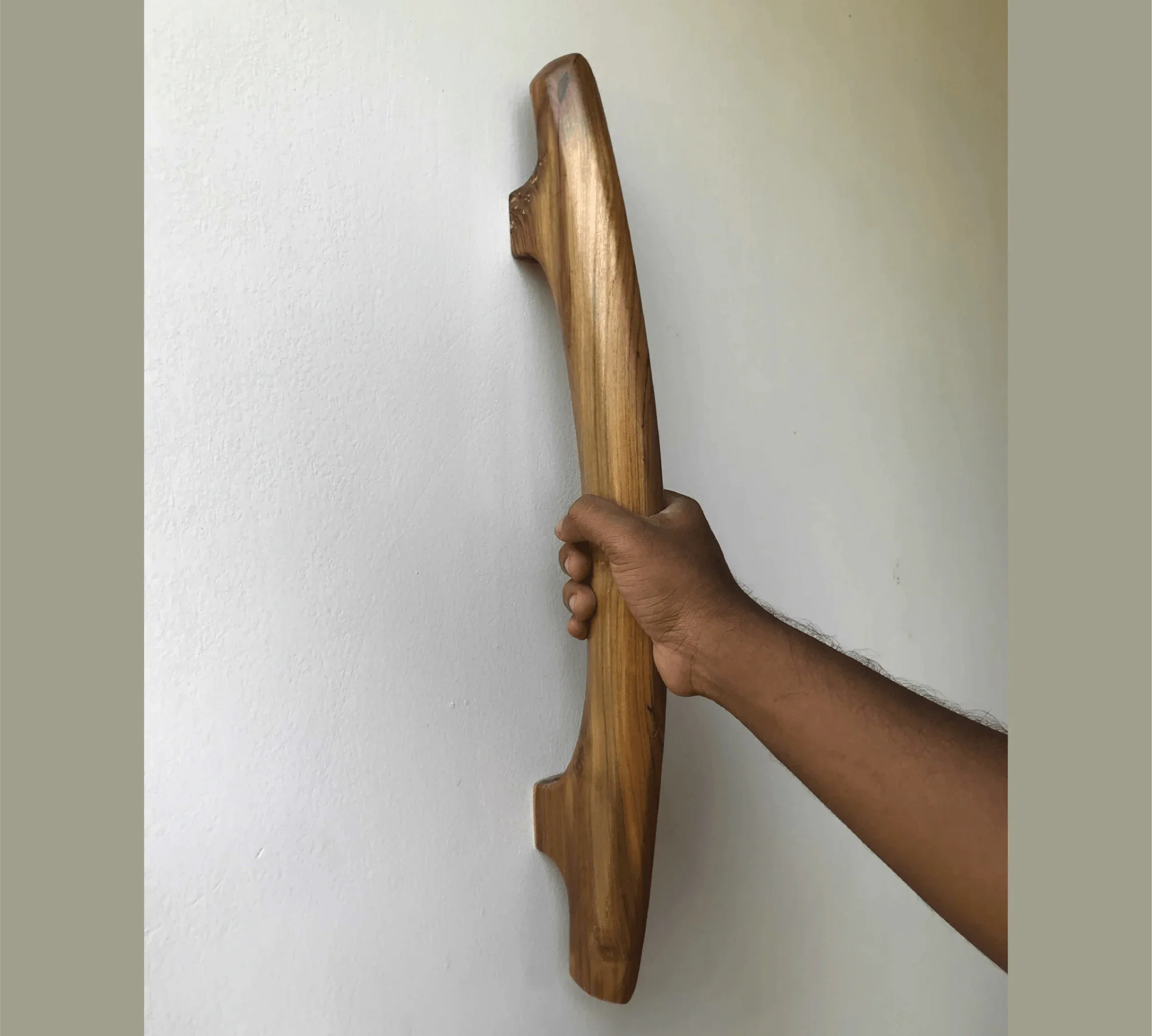Hand holding a handmade teak door handle mounted on a white wall by Wood Ceylon