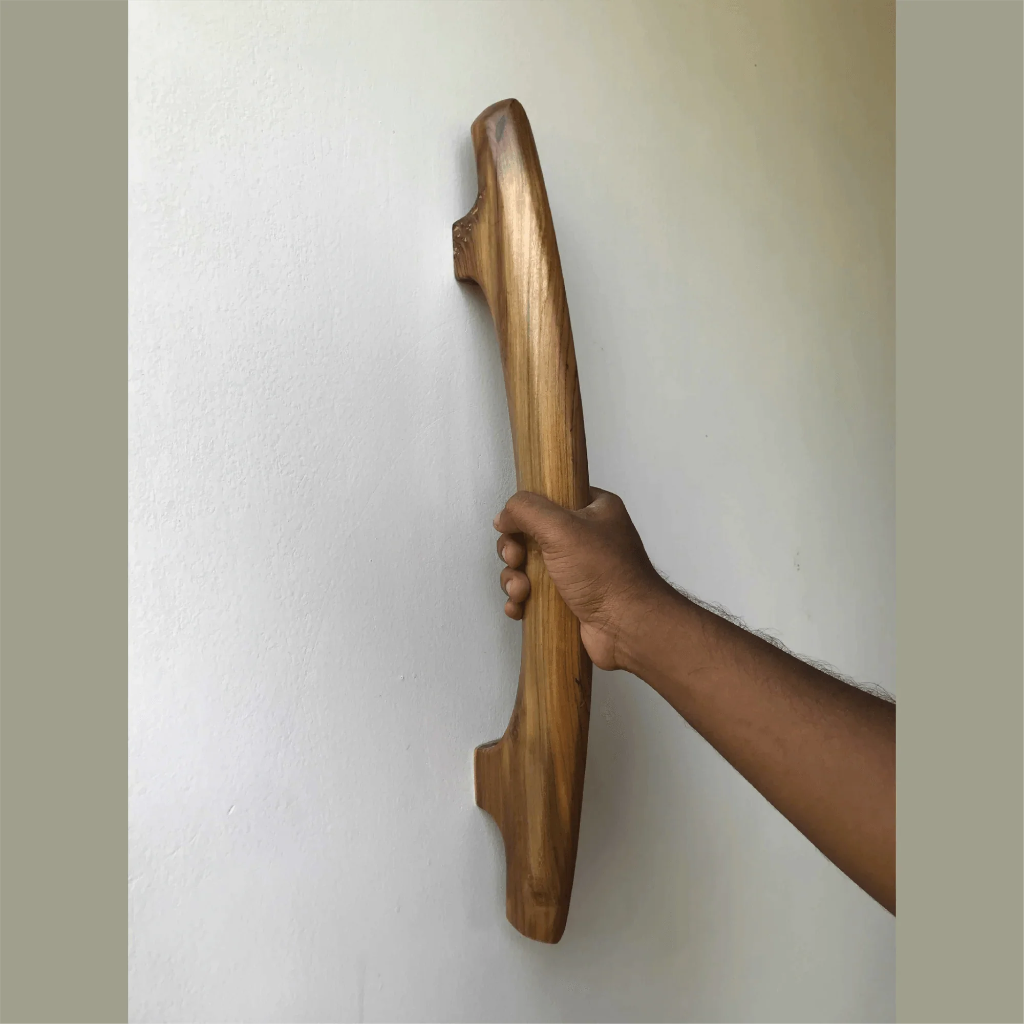 Hand holding a handmade teak door handle mounted on a white wall by Wood Ceylon