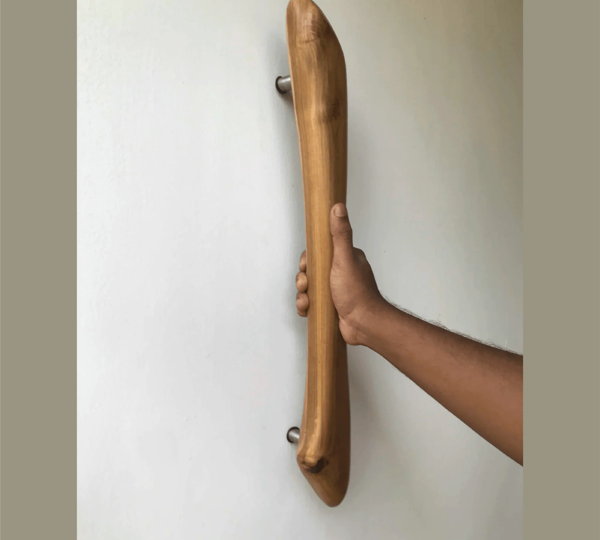 Hand gripping smooth curved wooden front door handle mounted on white wall by Wood Ceylon